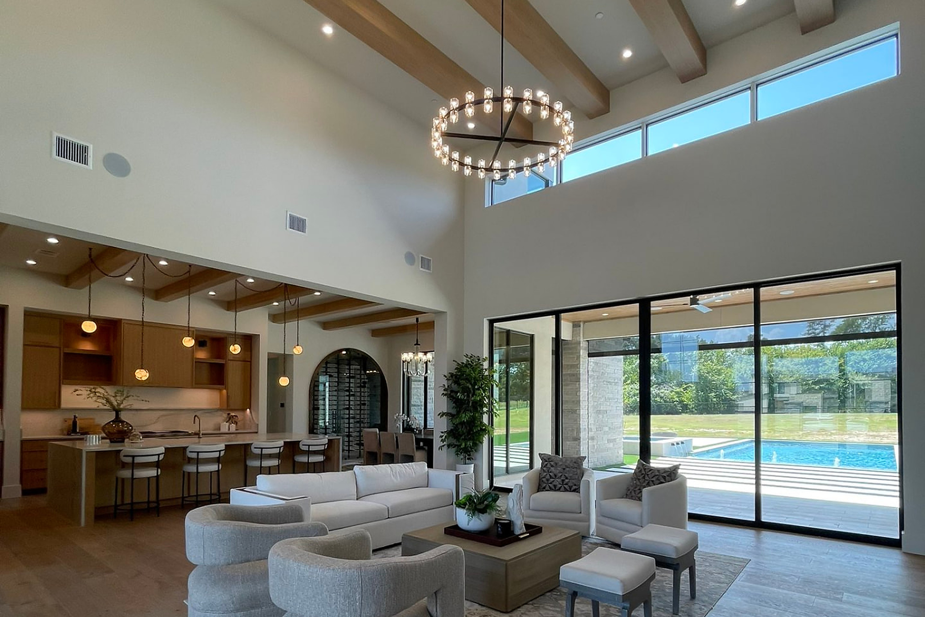 Open-plan luxury great room with vaulted timber beams and pool beyond